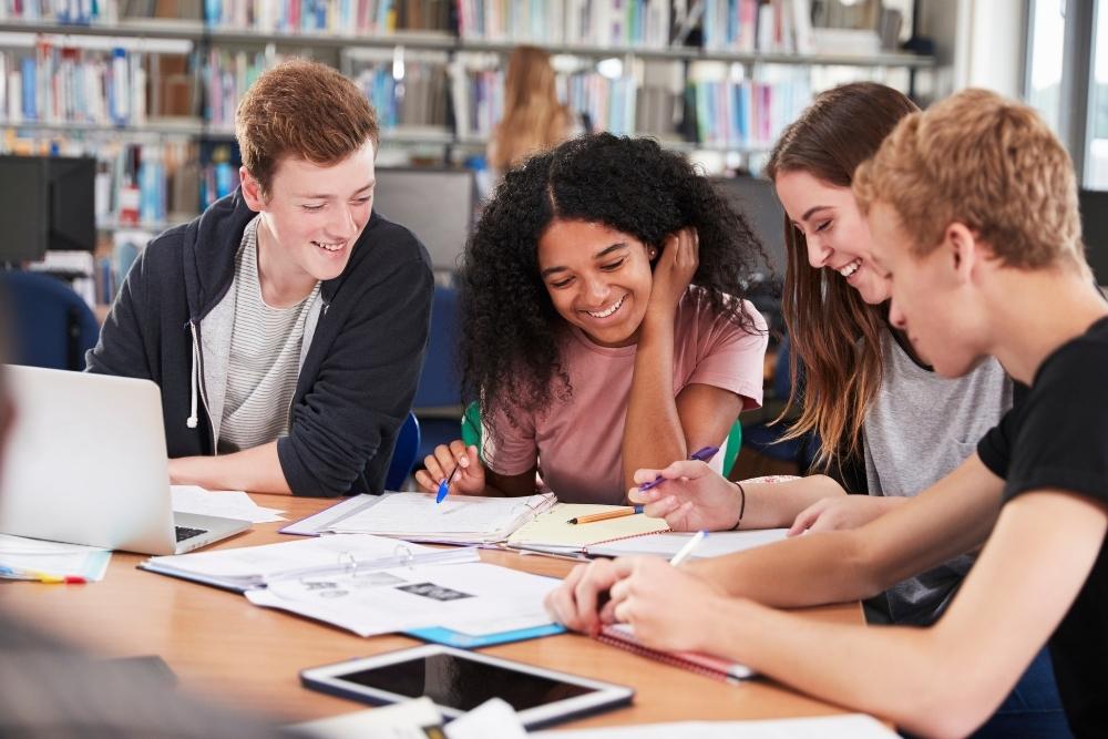 estudantes do ensino médio sorrindo e estudando em grupo na biblioteca escolar.