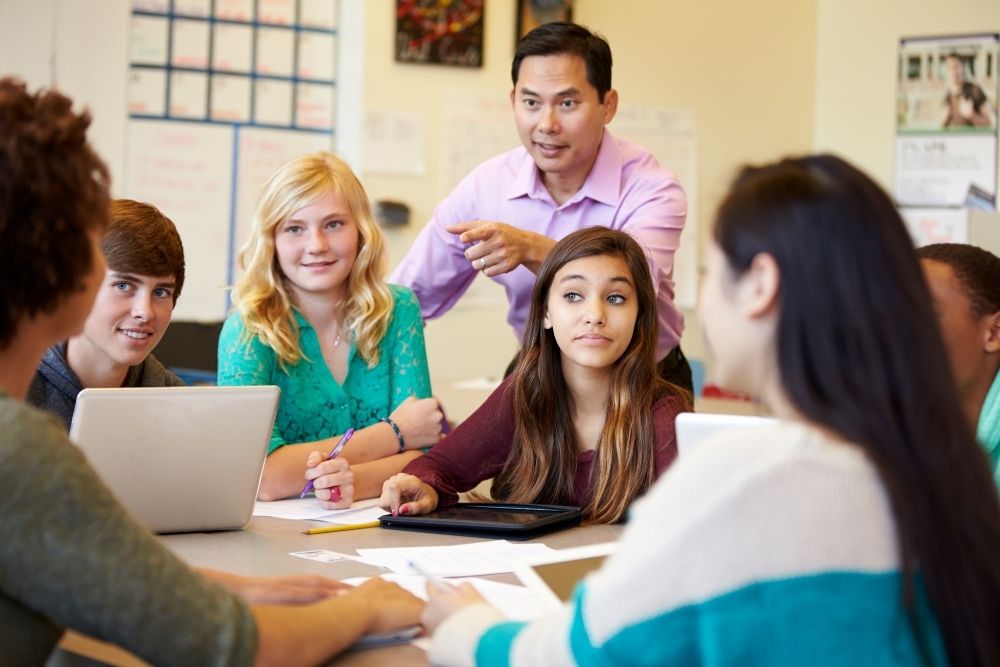 professor orientando grupo de alunos do ensino médio durante atividade em sala.