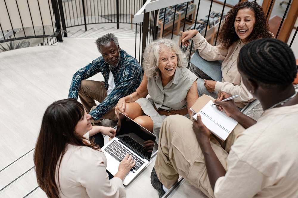 pessoas diversas reunidas em escada, sorrindo e conversando com anotações e laptop.