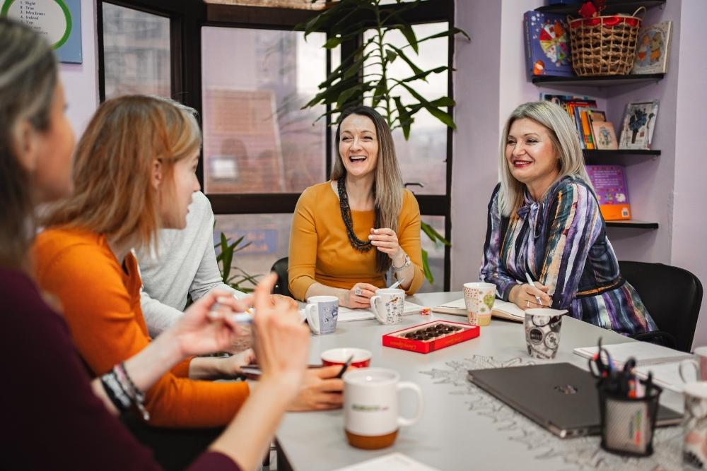 grupo de mulheres conversando alegremente em uma mesa com café e doces.