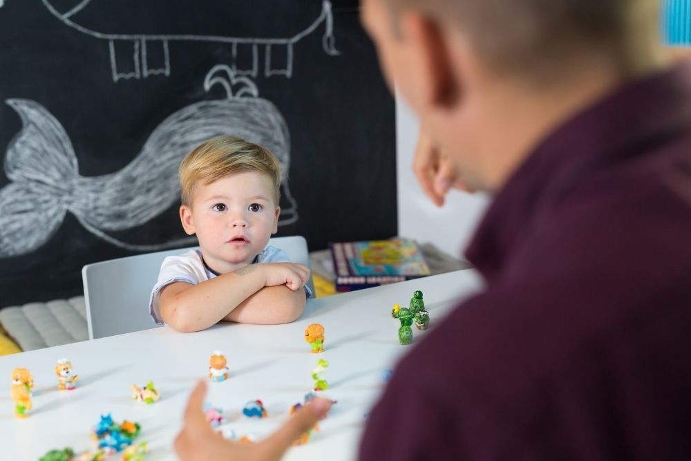 Menino atento interagindo com educador em sala de aula com brinquedos educativos.