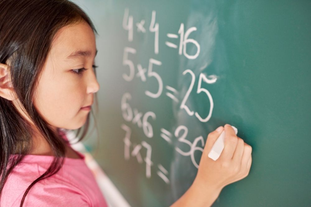 Criança aprendendo multiplicação na lousa durante aula de matemática na educação infantil.