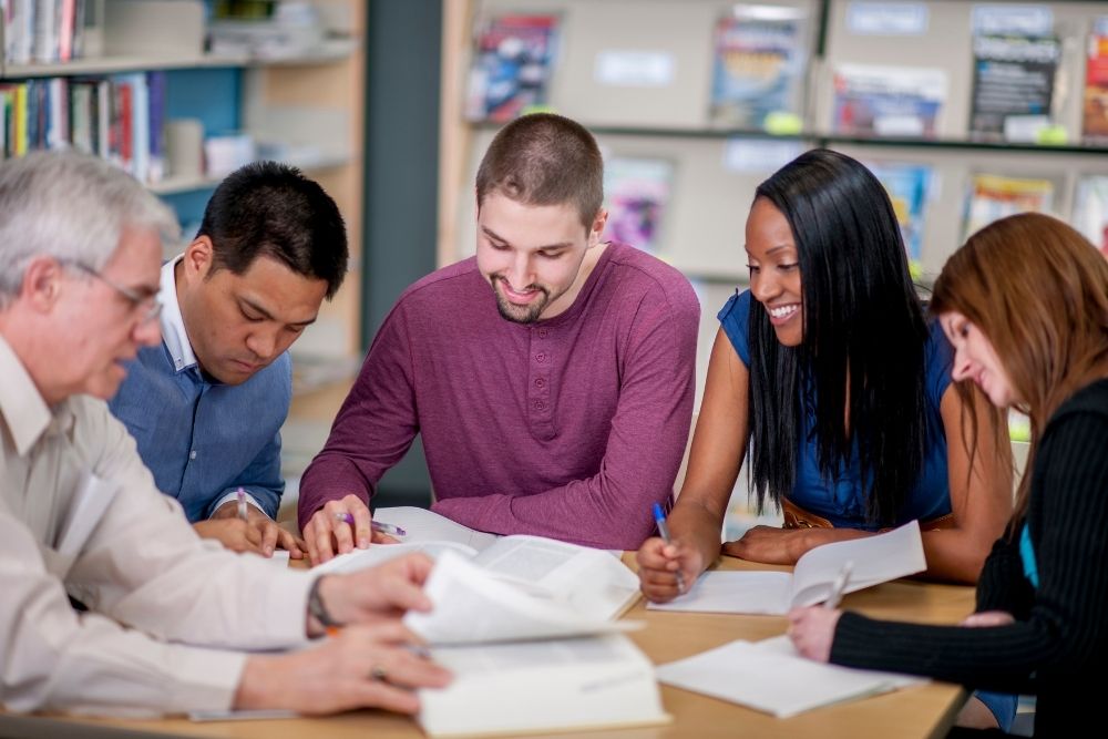 grupo diverso de educadores estudando juntos em uma biblioteca escolar.