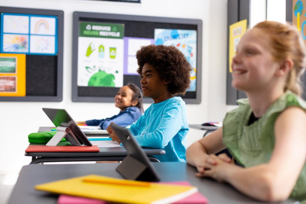 Crianças sorrindo em sala de aula enquanto usam Tablets para estudar.