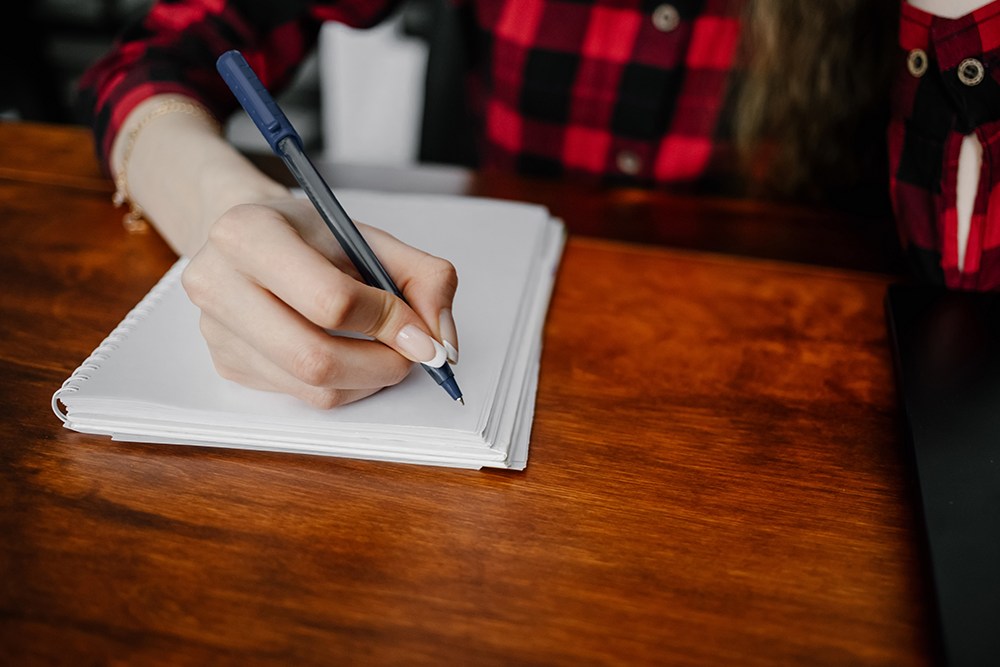 mão de mulher escrevendo com caneta em folha branca de caderno.