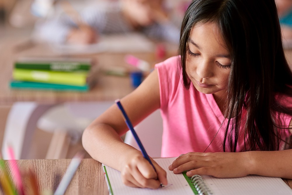 Aluna de ensino fundamental em sala de aula escrevendo em um caderno.