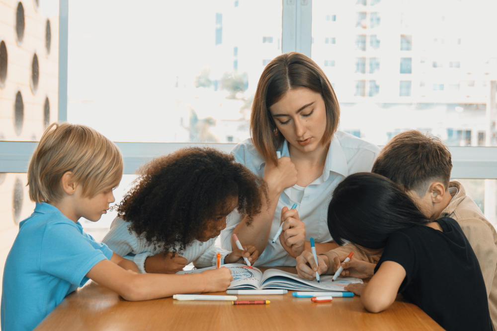 Grupo de alunos colorindo o mesmo caderno em frente à professora