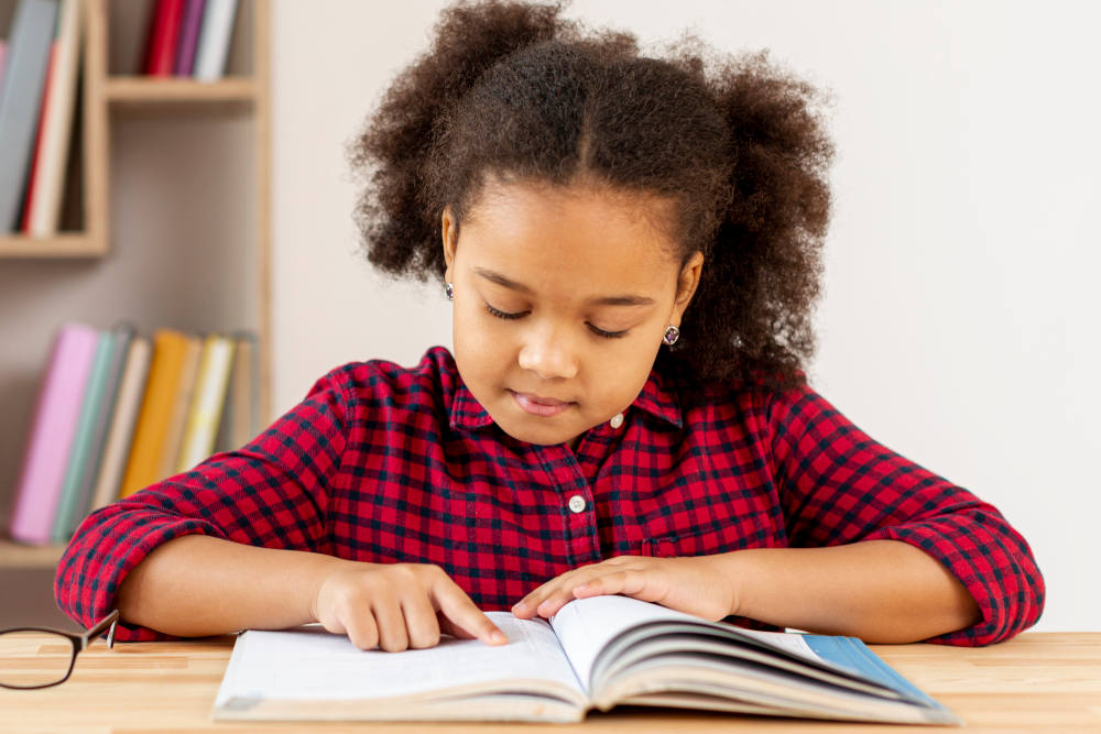 Menina usando camisa xadrez vermelha lendo um livro didático sobre a mesa