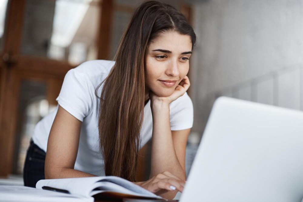 Aluna do ensino médio usando computador para estudar e fazendo anotações em sua apostila.