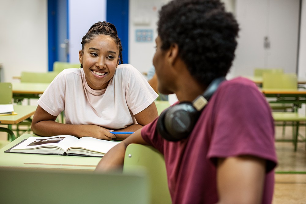 Colegas de classe conversando em sala de aula enquanto estudam.