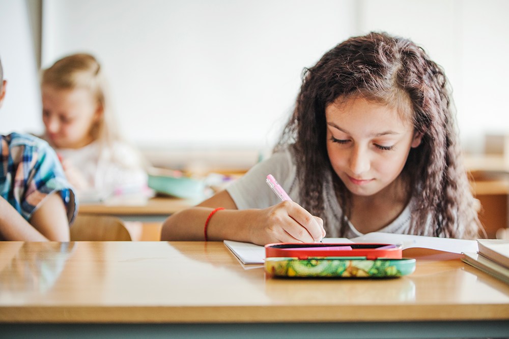 Aluna do ensino fundamental na sala de aula escrevendo em seu caderno.