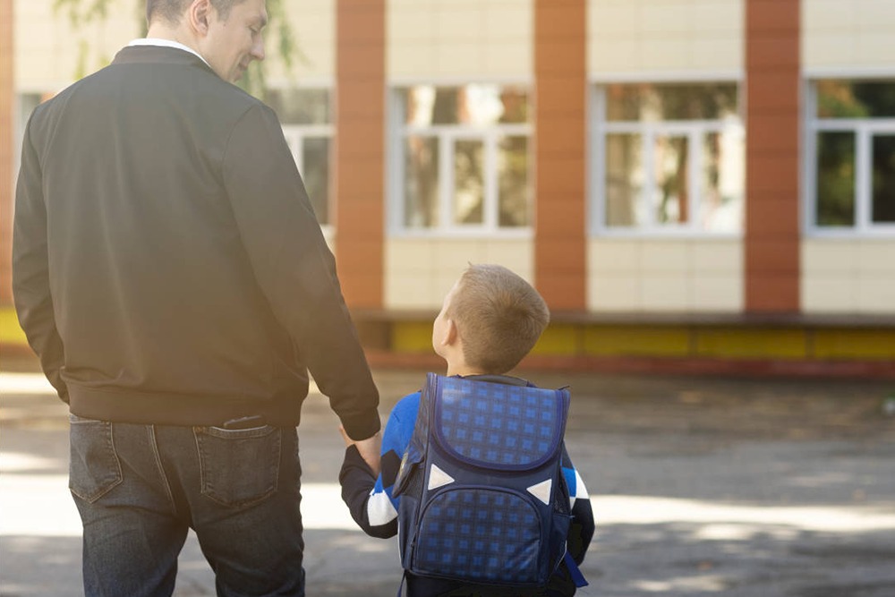 Pai e filho pequeno de costas andando de mãos dadas a caminho da escola.